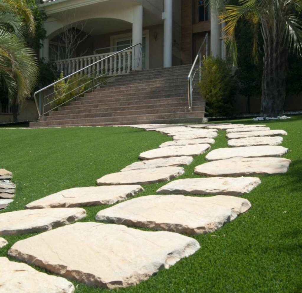 Camino de piedra natural integrado en césped artificial en un jardín volcánico